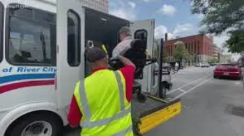Public transportation driver helping a man in a power wheelchair to get onto a bus using a lift