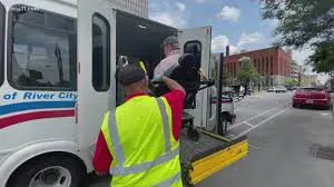 Public transportation driver helping a man in a power wheelchair to get onto a bus using a lift