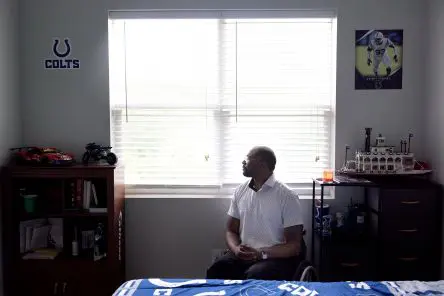 Terrell is a Black man sitting in a manual wheelchair in his bedroom and looking out the window.