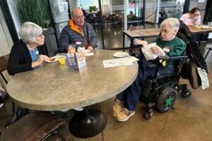 Three individuals enjoying food and conversation at a round table in a cozy space.