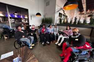 Group of women and men in wheelchairs smiling for a group photo in a festive venue.