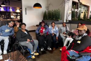 Close-up of group of women and men in wheelchairs, showcasing their smiles and camaraderie in a welcoming space.