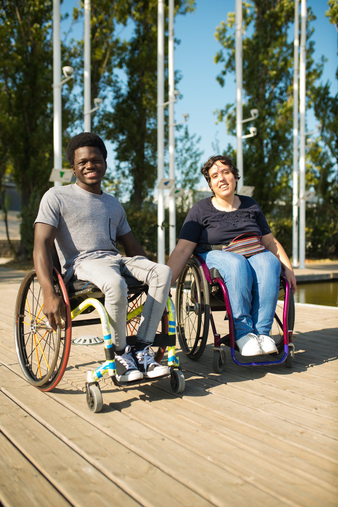 dreamstime_m_259751821 A young black man and young white woman are sitting in manual wheelchairs at a public park.