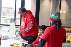 A man wearing a red Santa hat and shirt getting food from a catering buffet.