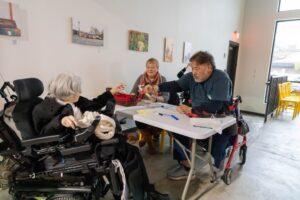 eople gathered around a table playing a game, including an attendee using a power wheelchair.